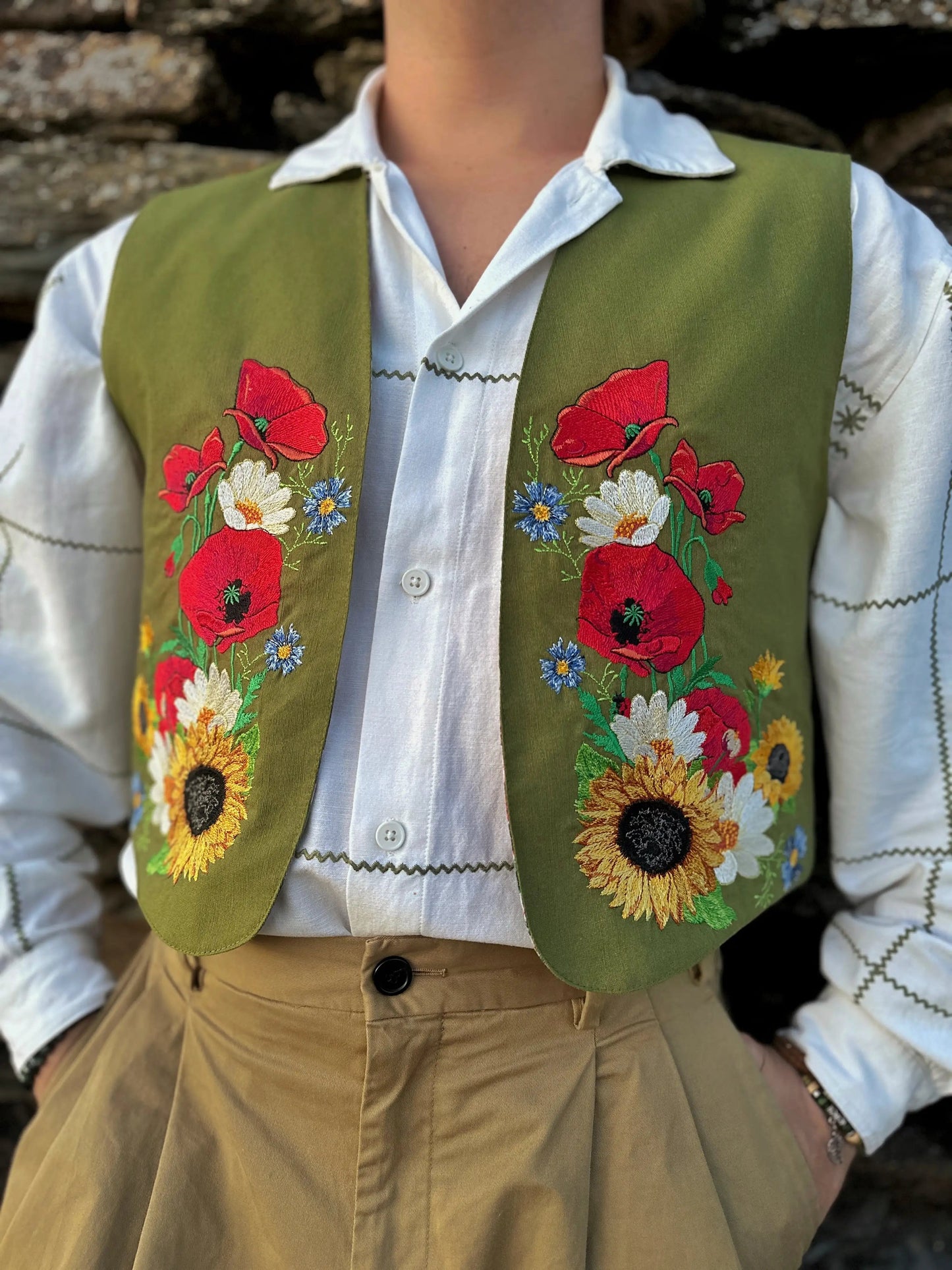 Person wearing a green vest with floral embroidery over a white shirt.