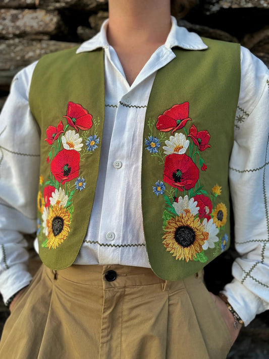 Person wearing a green vest with floral embroidery over a white shirt.