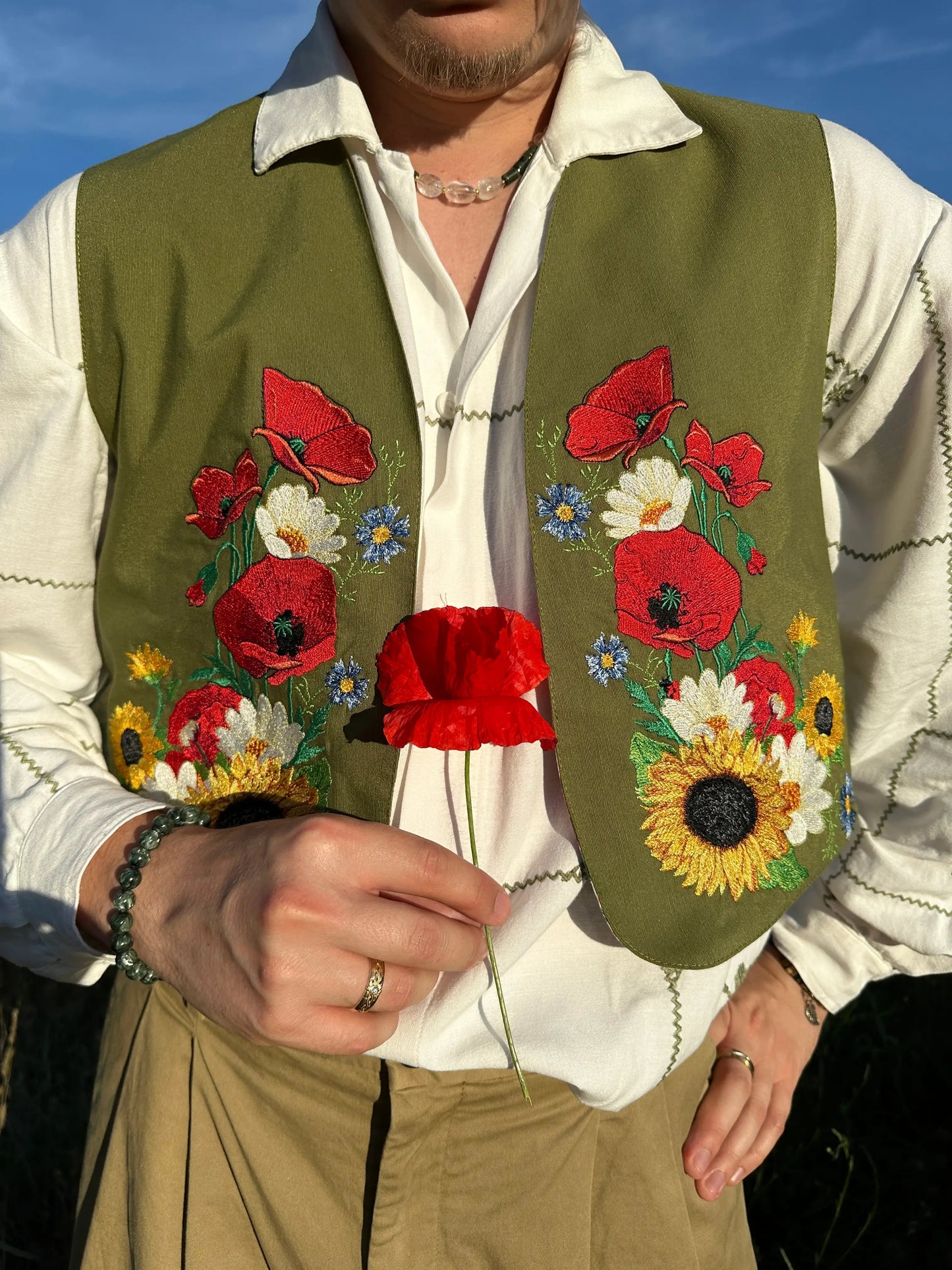Person wearing a green vest with floral embroidery against a blue sky.