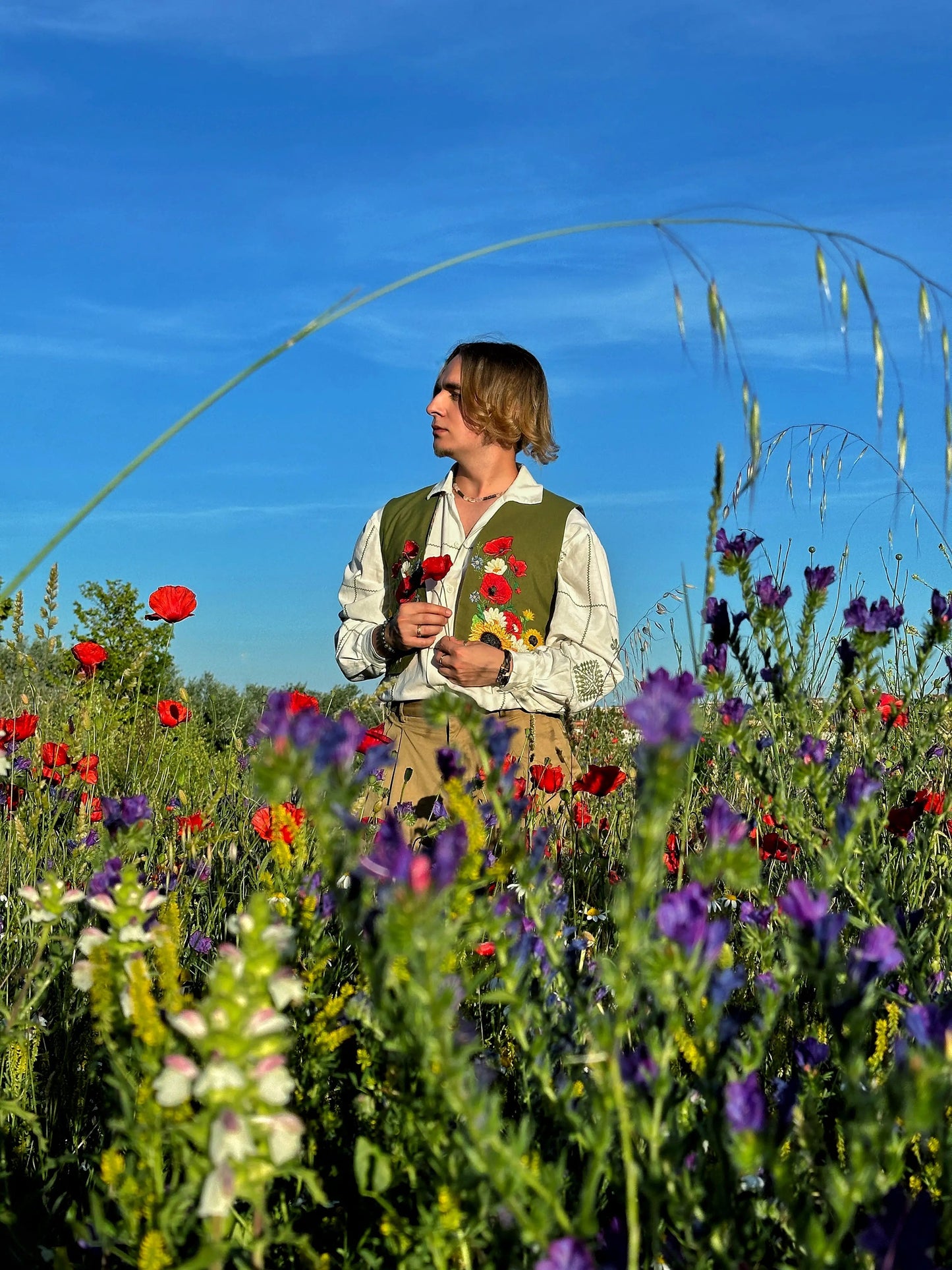 Man standing in a field of wildflowers with a clear blue sky.