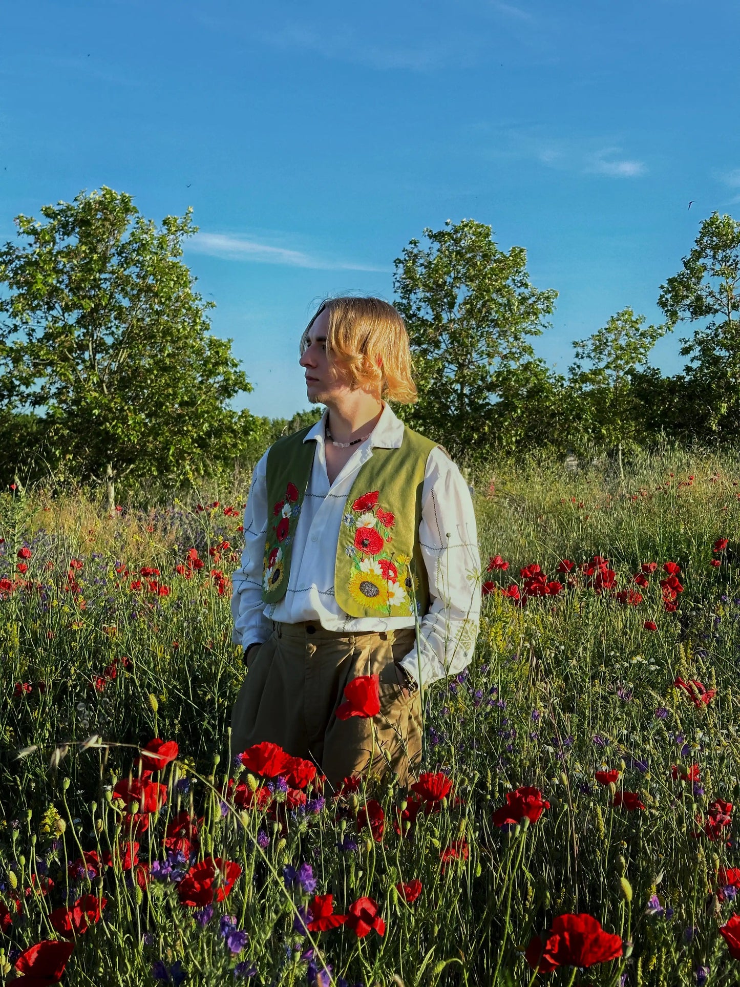 Person standing in a field of flowers with trees and blue sky in the background