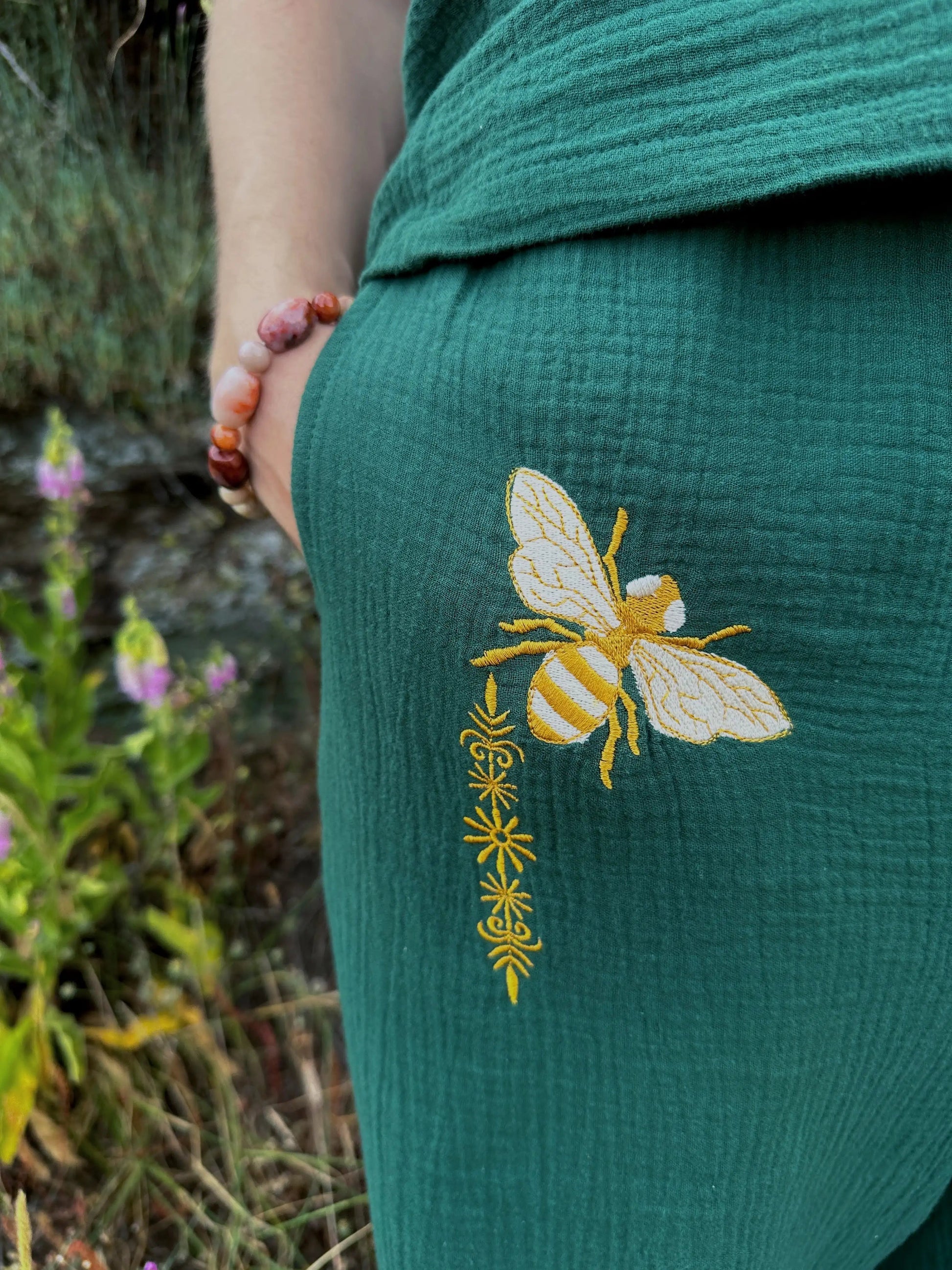 Green garment with a yellow bee design embroidered on it, held by a person in a natural setting.