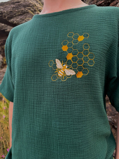 Green shirt with embroidered bee and honeycomb design worn by a person outdoors.
