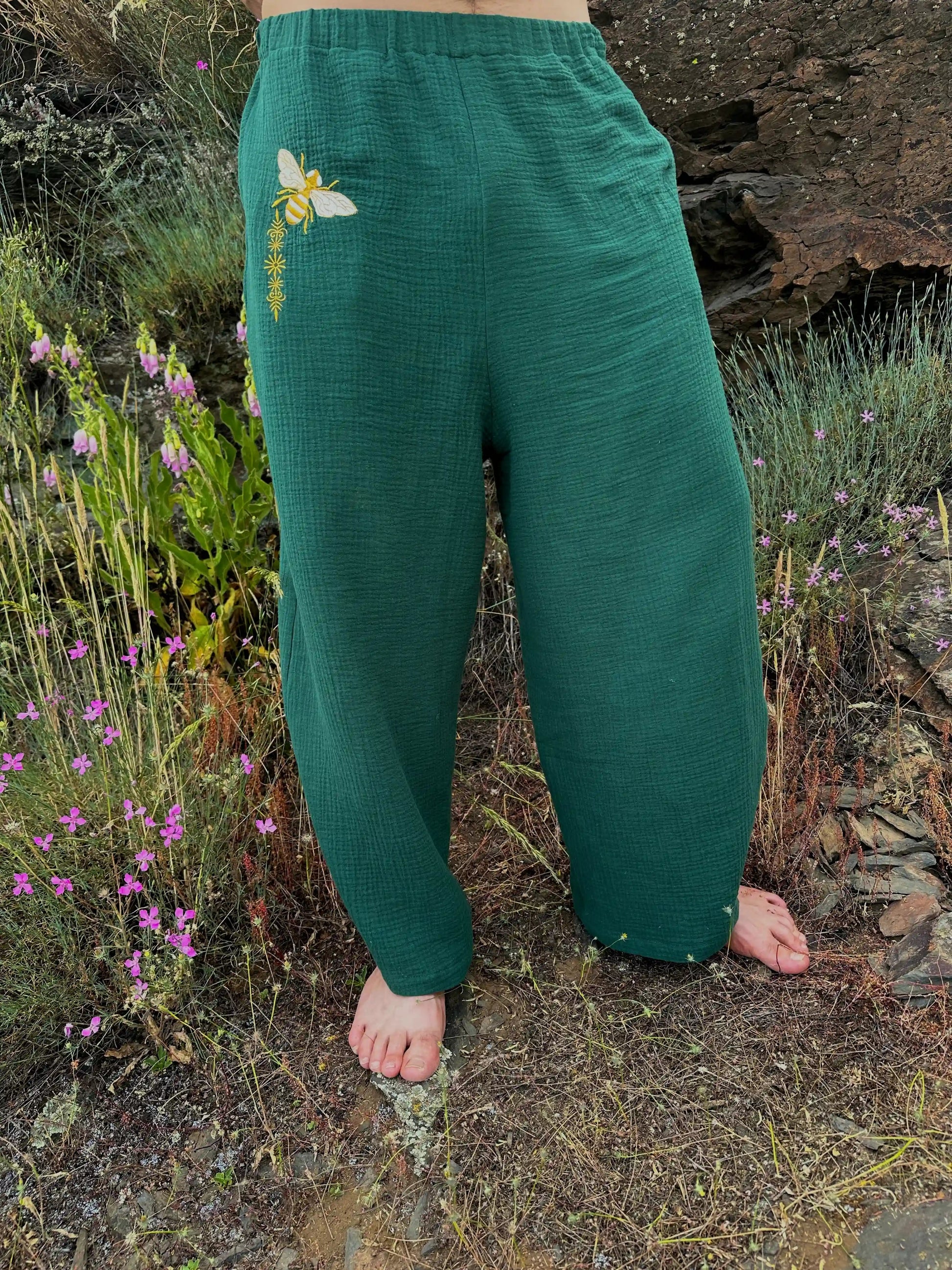 Green pants with a floral design worn by a person standing in a natural setting with plants and rocks.