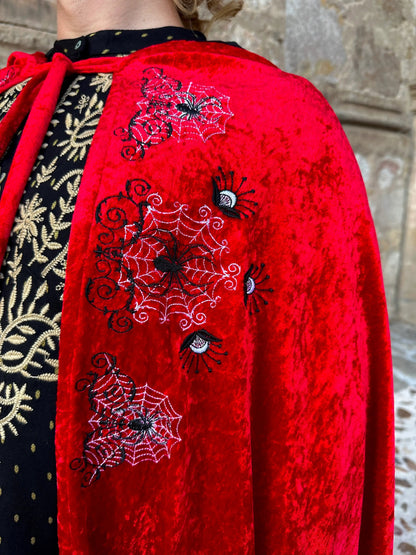 Red garment with spider web and eye embroidery against a stone wall background