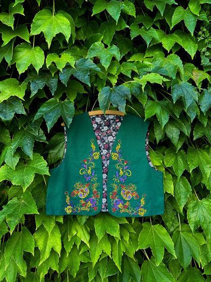 Green embroidered vest hanging against a green leafy background
