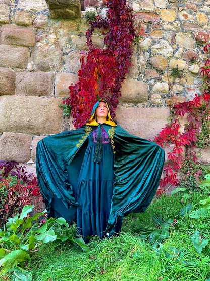 Person in a teal cloak standing in front of a stone wall with red foliage