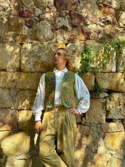 Person wearing a traditional outfit with a colorful vest against a stone wall.