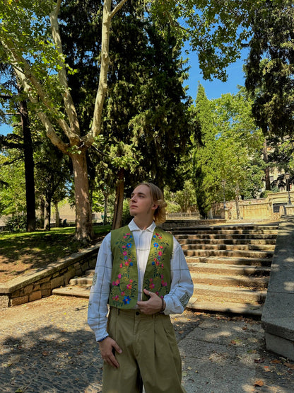 Person wearing a patterned vest standing in a park with trees and steps in the background