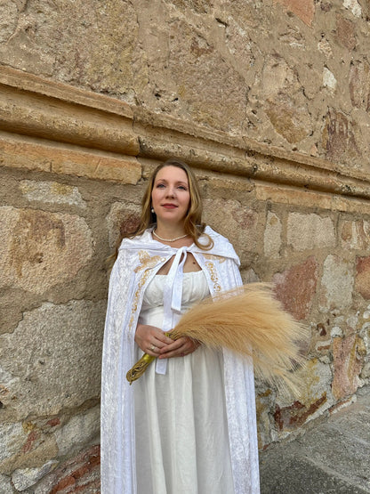Woman in a white dress with a long, light-colored train standing against a stone wall.