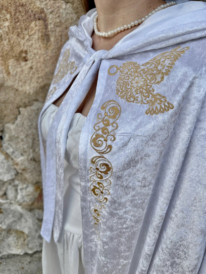 White shawl with gold embroidery draped over a person against a stone wall.