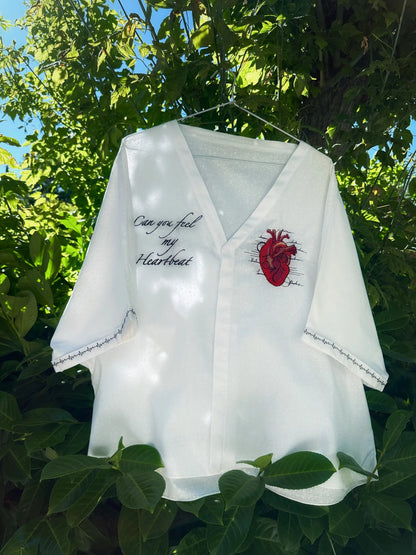 White shirt with red heart design and text hanging outdoors among green leaves