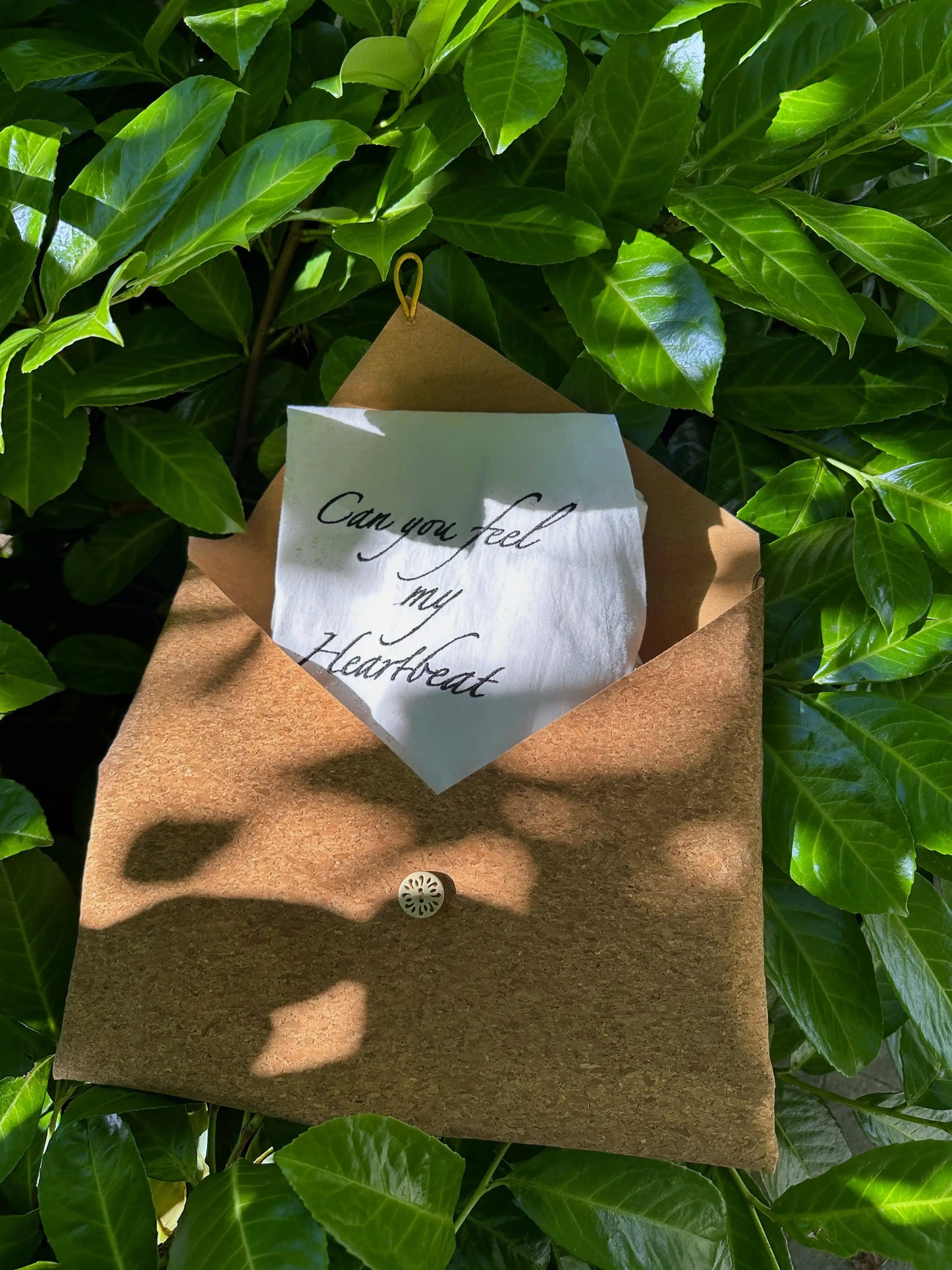 Brown envelope with a white card inside, hanging on green leaves