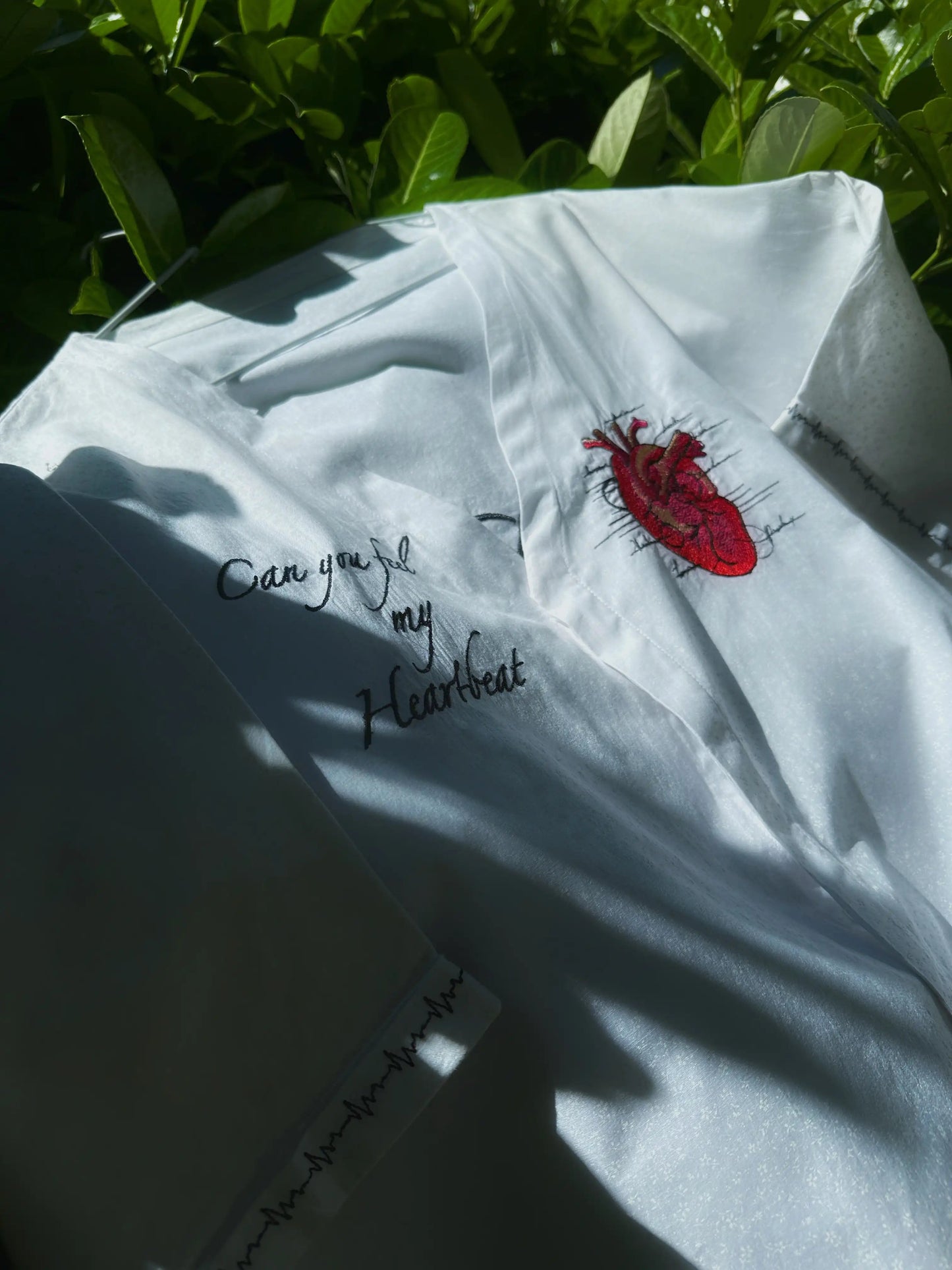 White shirt with red heart design and text on a green leafy background