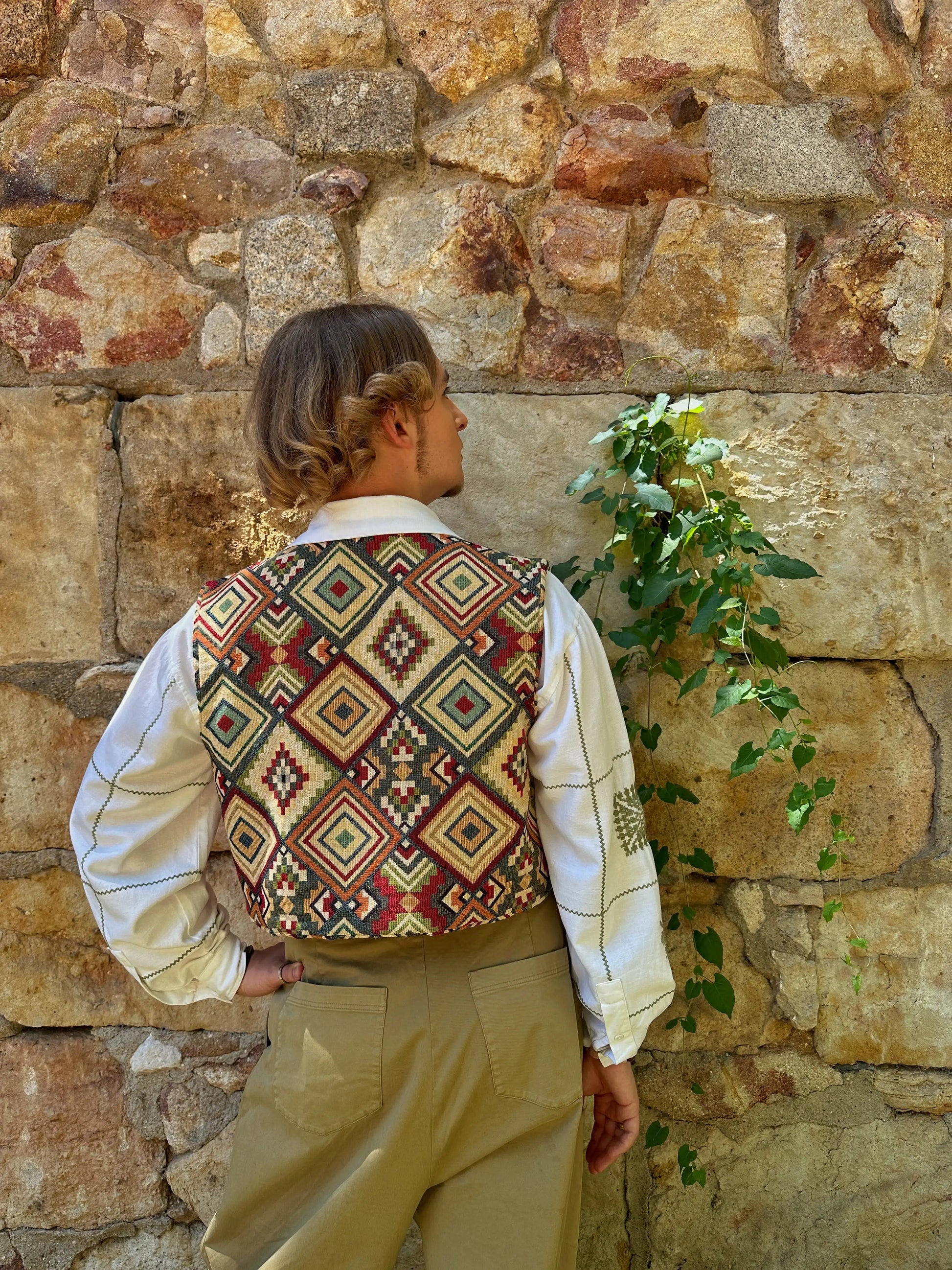 Person wearing a patterned vest against a stone wall