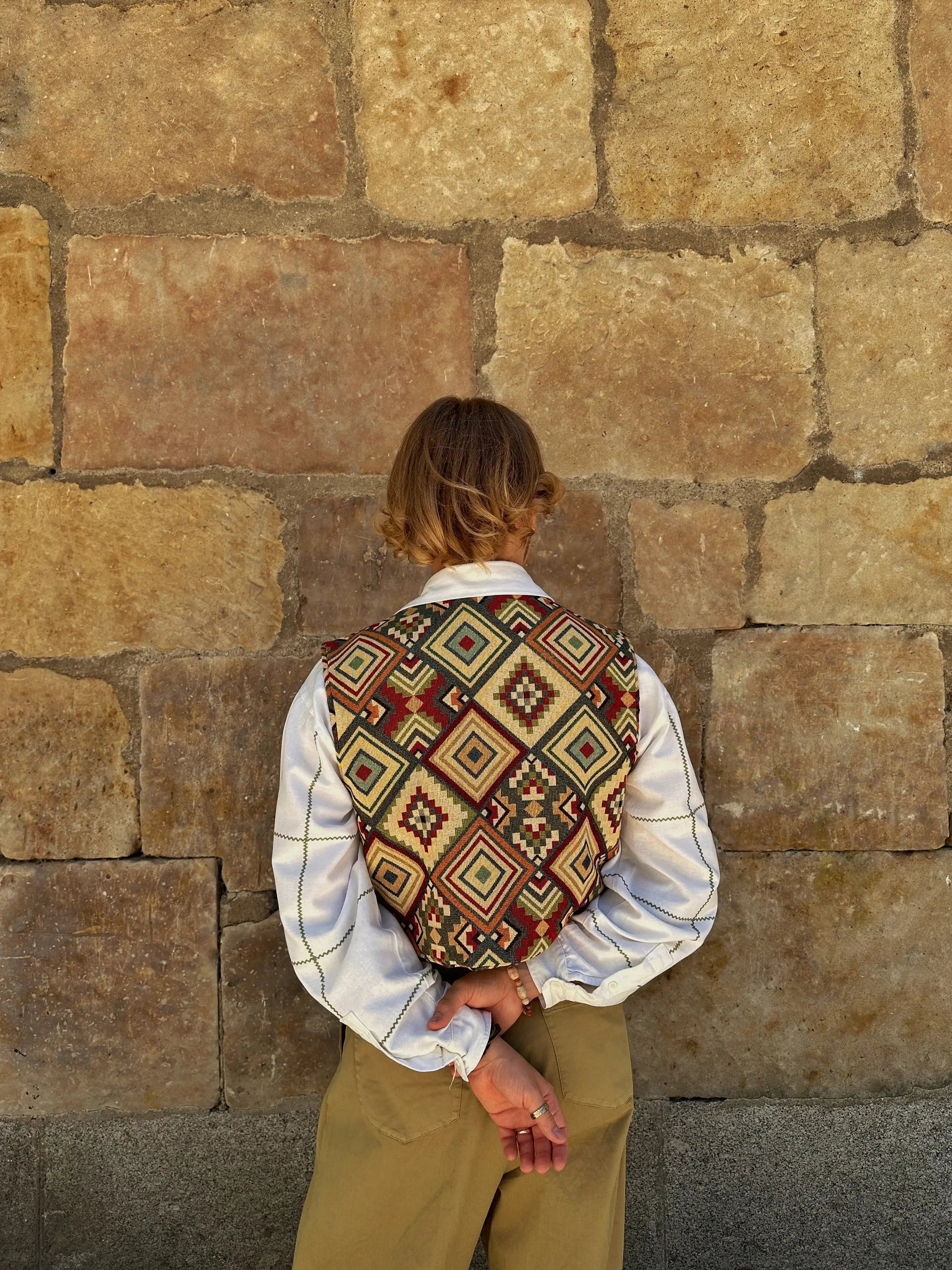 Person wearing a patterned vest against a stone wall