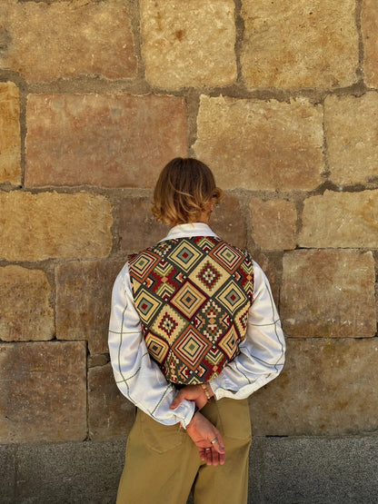 Person wearing a patterned vest against a stone wall