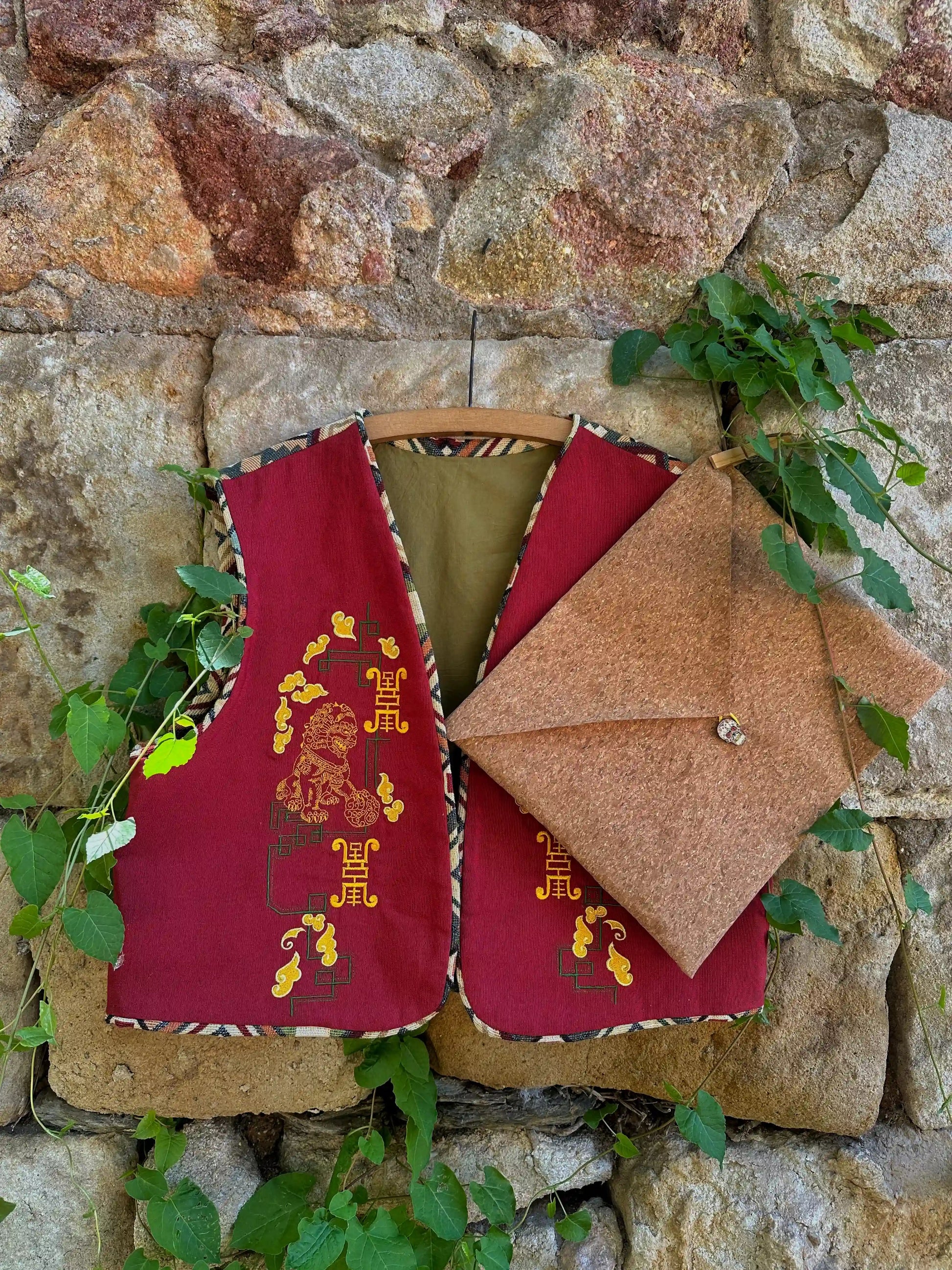 Red and brown fabric bags with embroidered designs hanging against a stone wall.