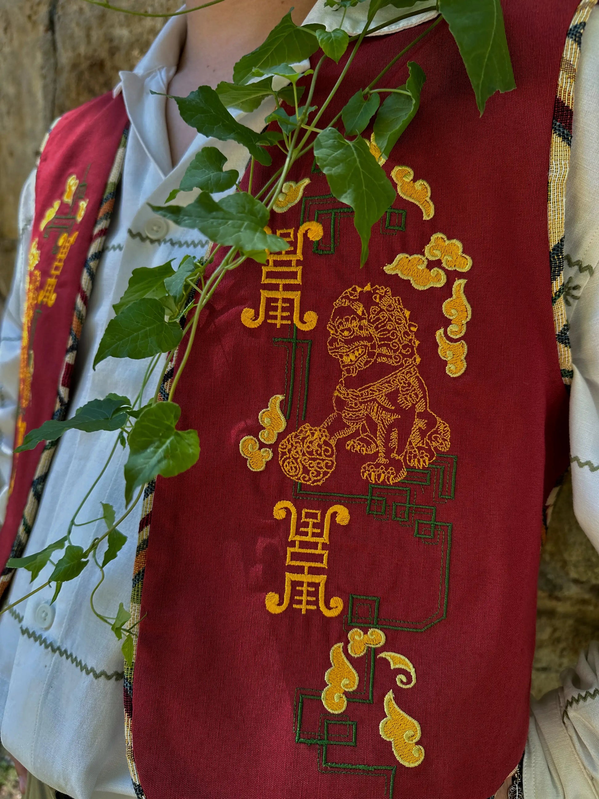 Red garment with gold embroidery featuring a lion design and Chinese characters, worn by a person.