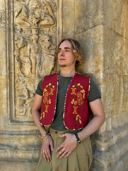 Person wearing a red vest with gold embroidery against a stone wall with carvings