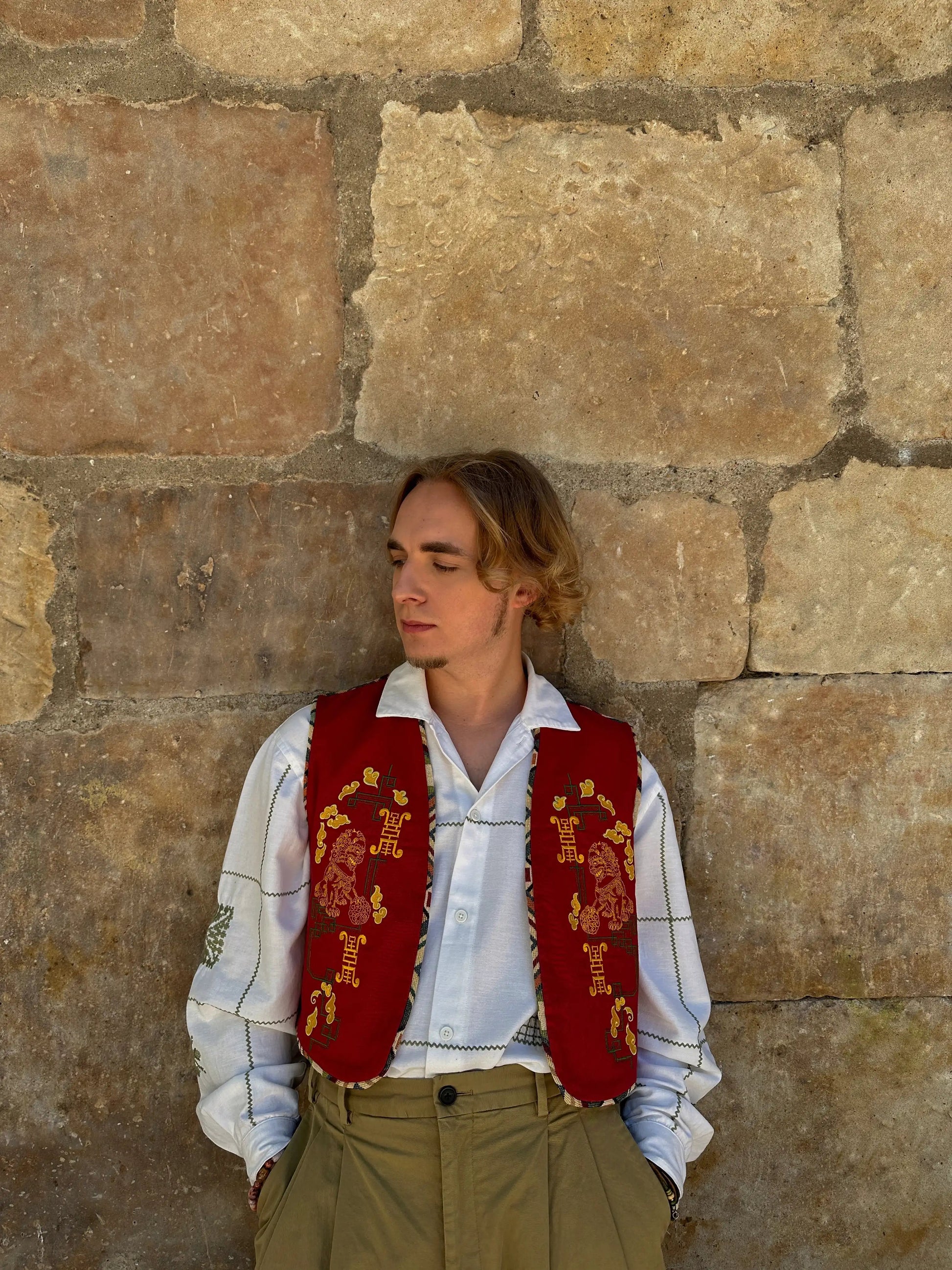 Person wearing a red embroidered vest against a stone wall