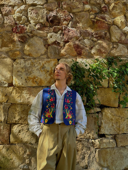 Person wearing a colorful embroidered vest against a stone wall