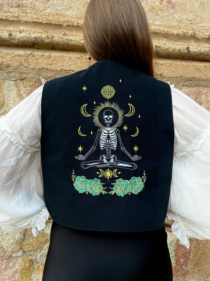 Person wearing a black vest with a skeleton design against a stone wall background