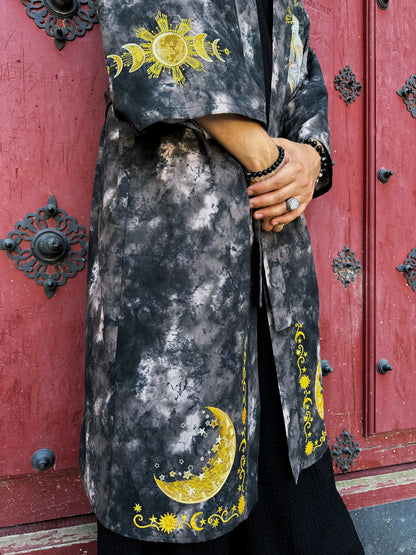 Person wearing a dark gray coat with yellow celestial designs in front of a red door.