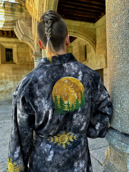 Person wearing a dark robe with a sun and tree design, standing in an architectural setting.