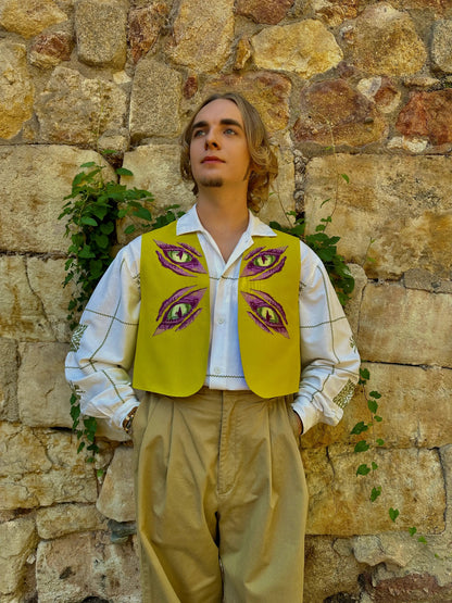Person wearing a yellow vest with eye designs against a stone wall.
