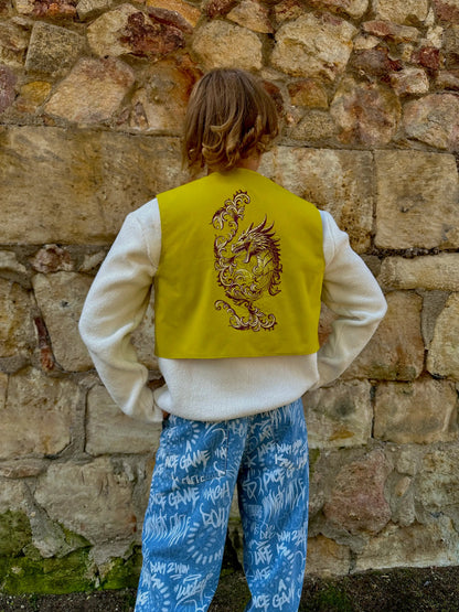 Person wearing a yellow vest with a dragon design against a stone wall.
