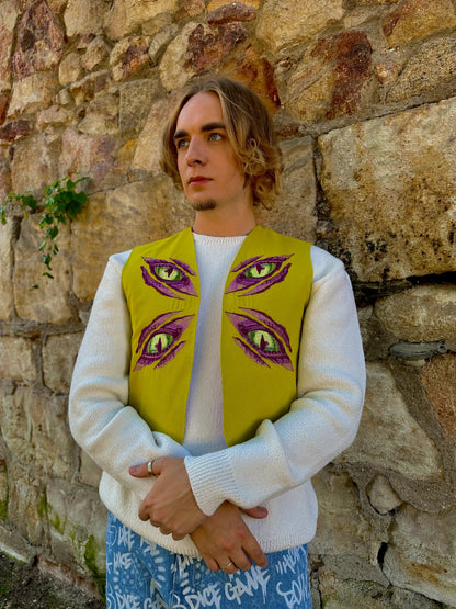 Person wearing a yellow vest with eye designs against a stone wall.