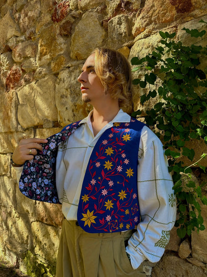Person wearing a colorful floral-patterned vest against a stone wall with greenery.