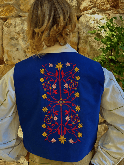 Person wearing a blue embroidered vest against a stone wall.