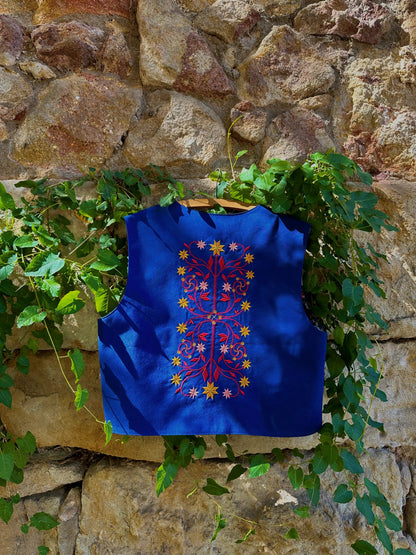 Blue embroidered vest hanging against a stone wall with greenery