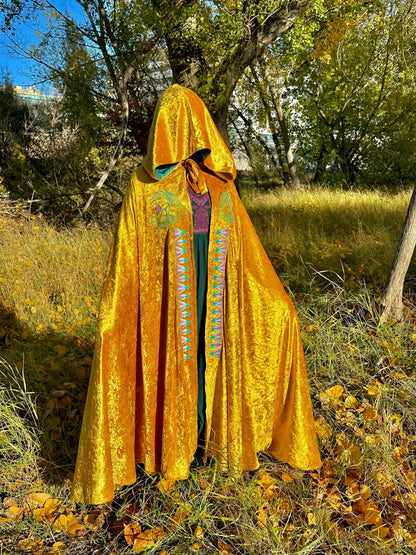 Person wearing a bright yellow embroidered cape in a natural setting with trees and grass.