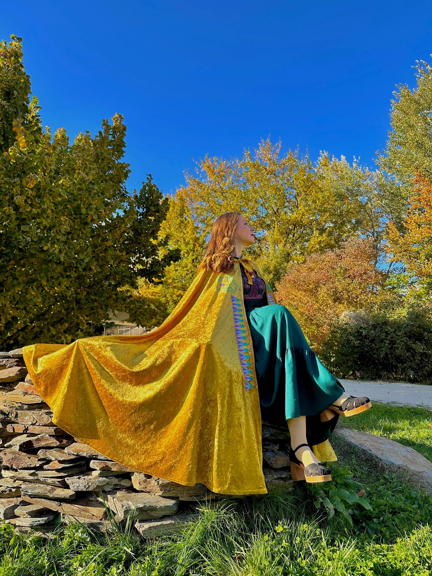 Person in a yellow and teal dress sitting on stone steps with trees and blue sky in the background