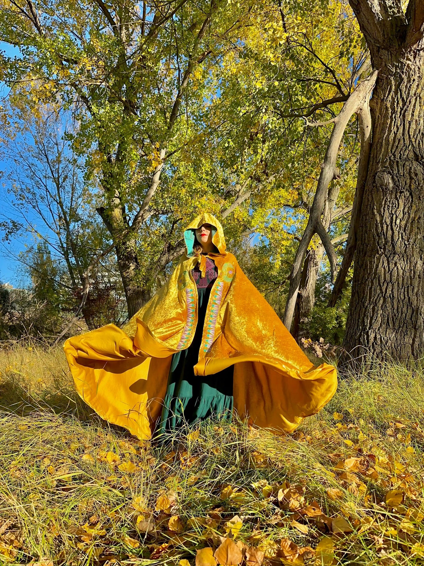 Person wearing a bright yellow hooded cloak in a forest with autumn leaves