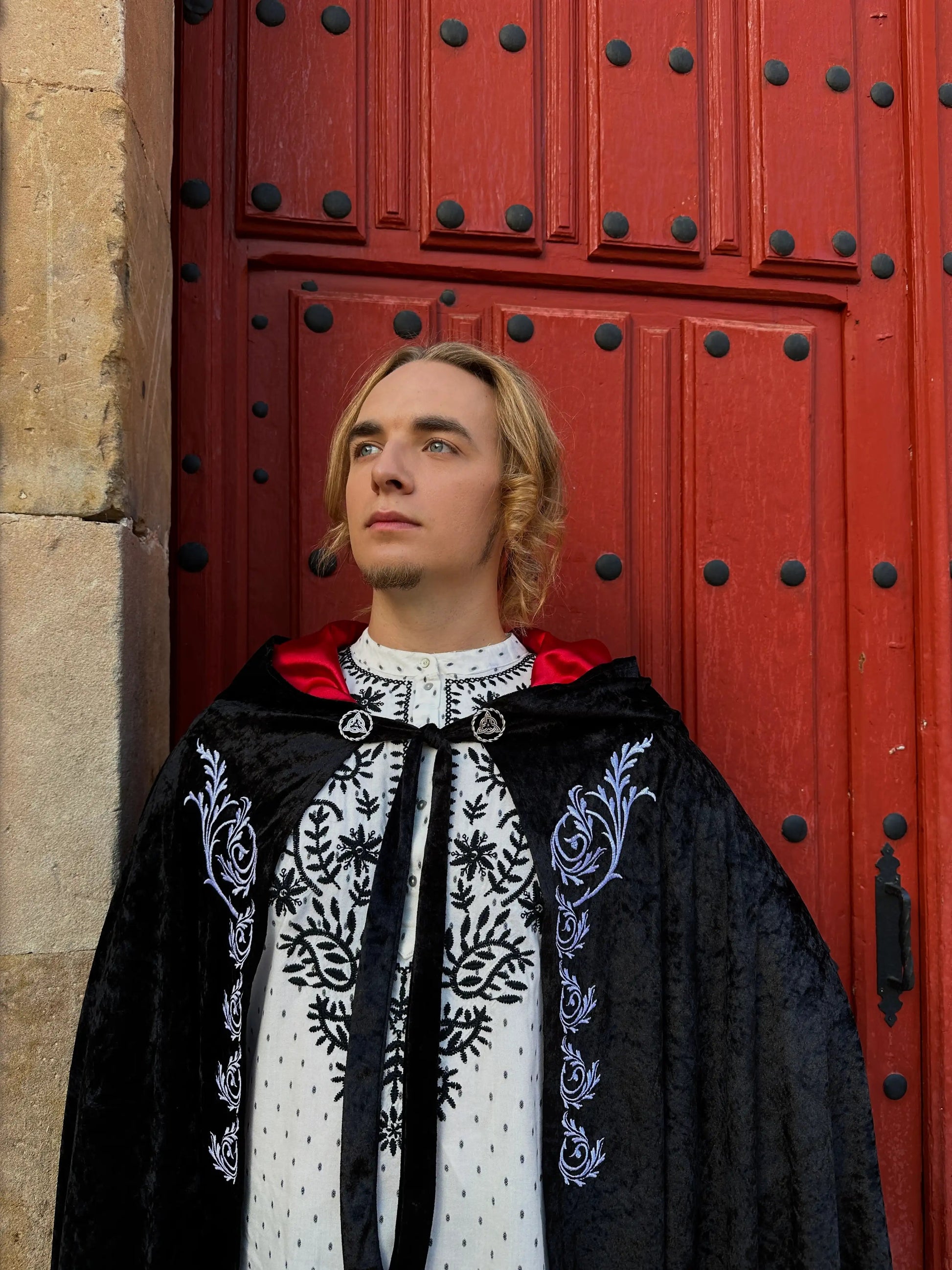 Person wearing a black embroidered cloak in front of a red door