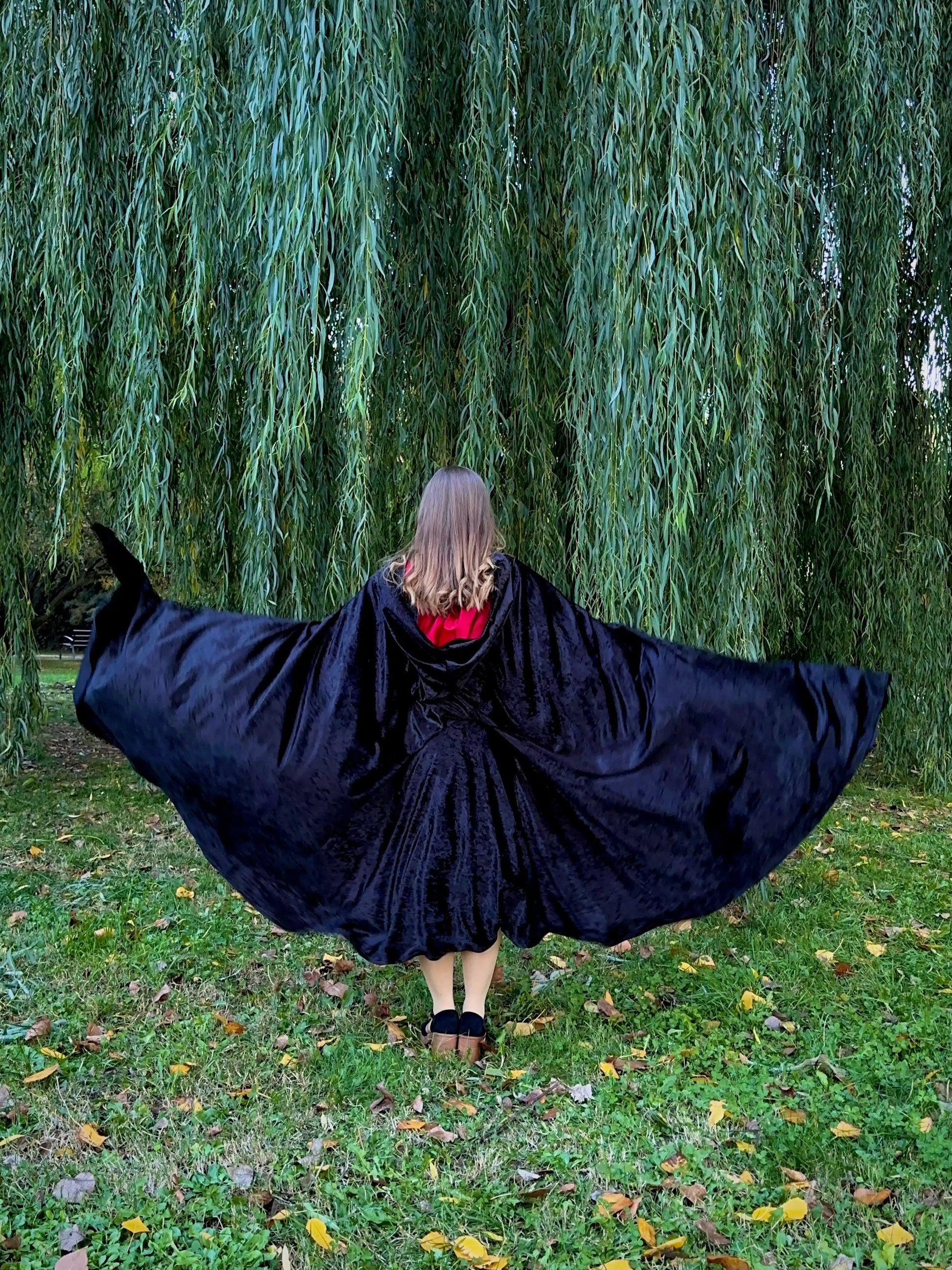 Person wearing a black cape in a park with willow trees