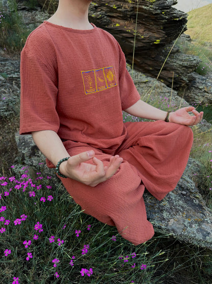 Person in a red outfit meditating outdoors with purple flowers and rocks in the background