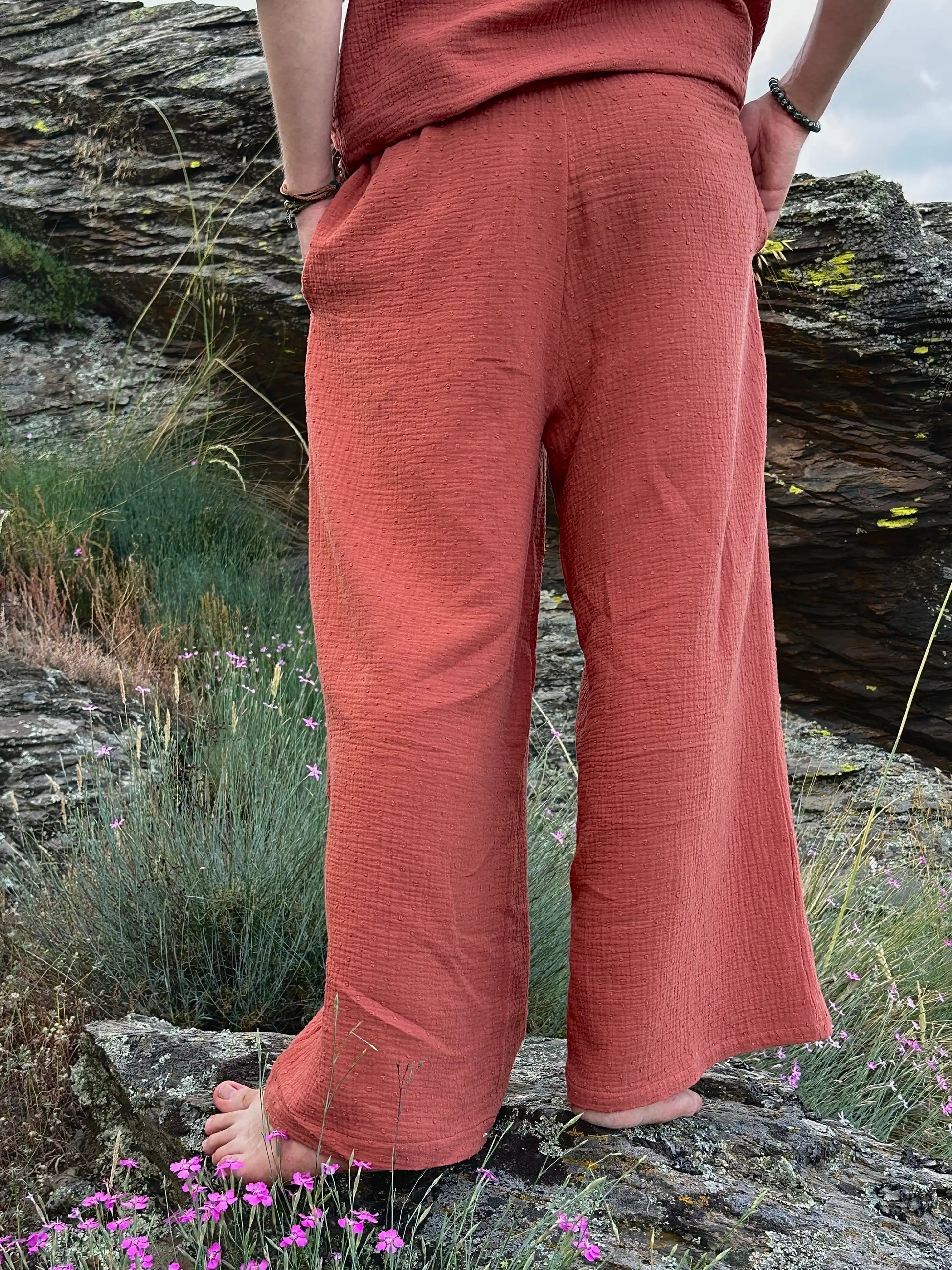 Person wearing a rust-colored outfit standing on rocks with grass and flowers in the foreground