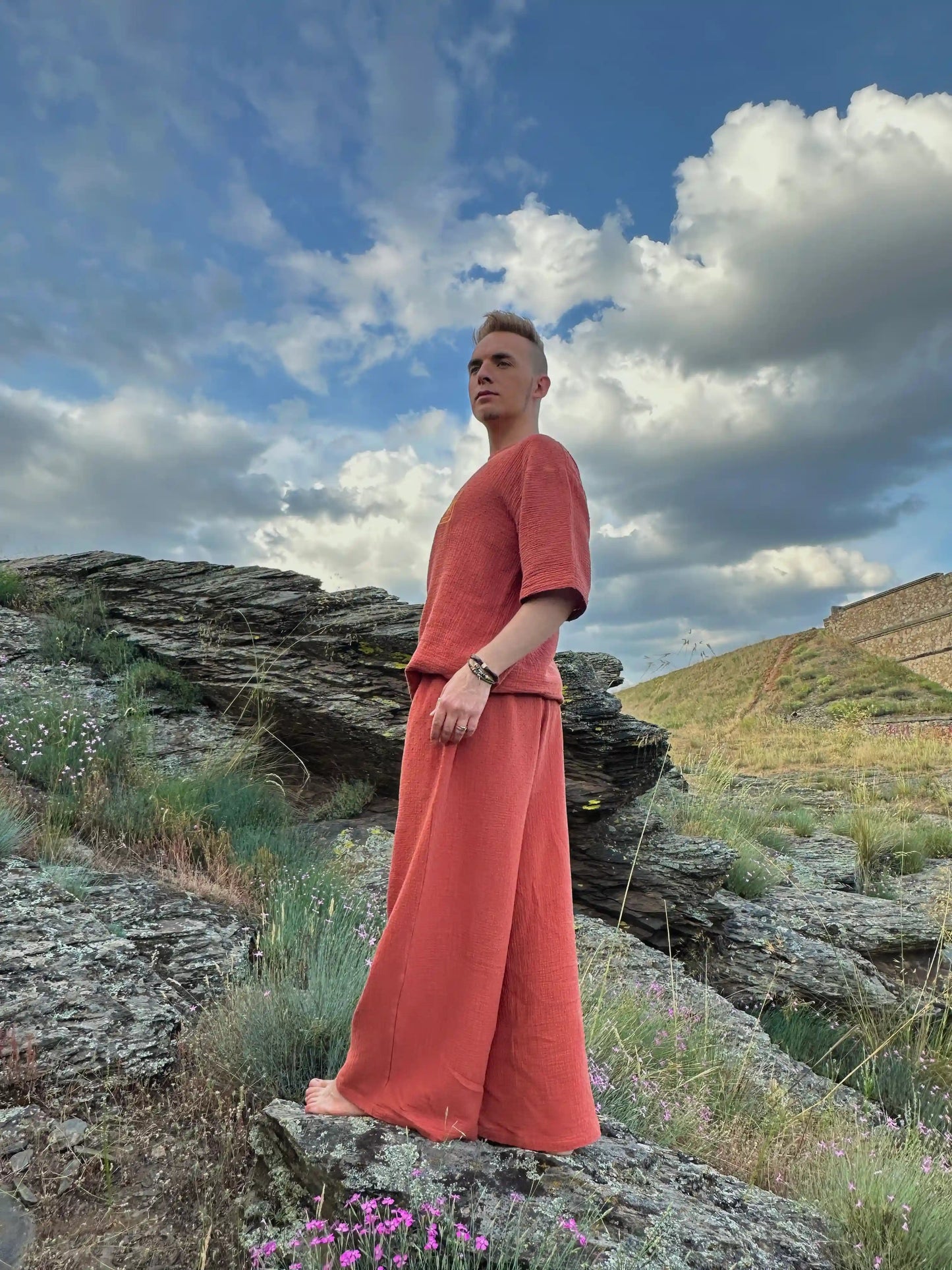 Person in a red outfit standing on a rocky landscape with a blue sky and clouds.