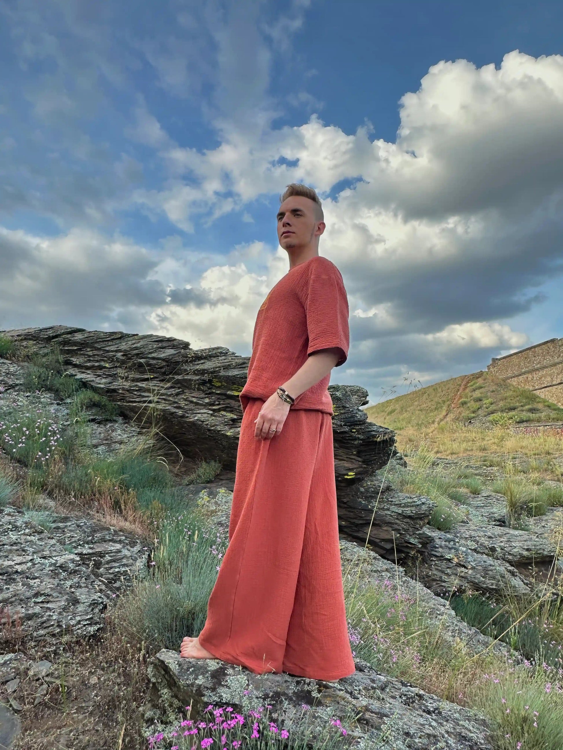 Person in a red outfit standing on a rocky landscape with a blue sky and clouds.
