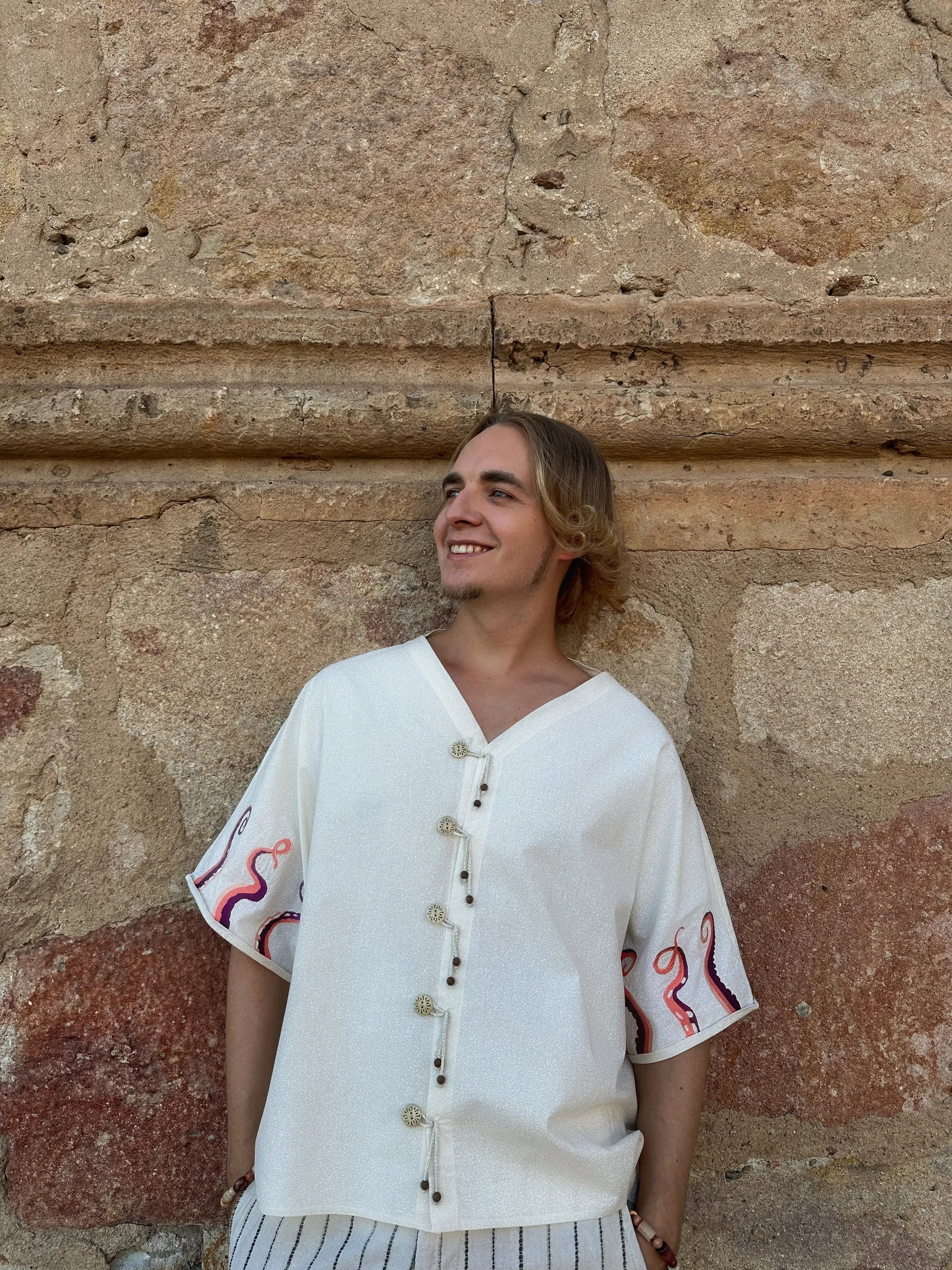 Person wearing a white embroidered shirt against a stone wall