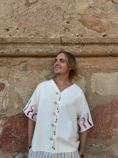 Person wearing a white embroidered shirt against a stone wall