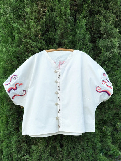 White embroidered blouse on a wooden hanger against a green bush background